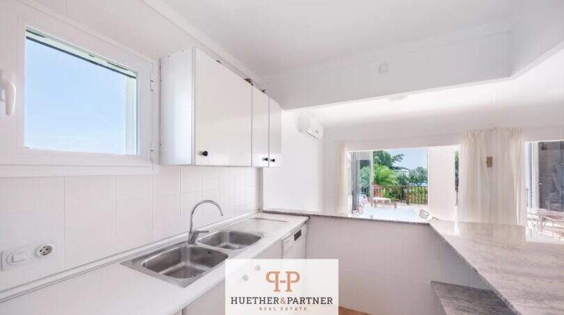 Helle weiße Einbauküche mit Doppelspüle und Durchreiche zum Wohnbereich mit Meerblick-Terrasse in Cala Mandía