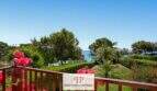Balkon mit Blumenreling, Gartenblick mit Palmen und türkisblauem Meer in erster Meereslinie, Cala Mandia