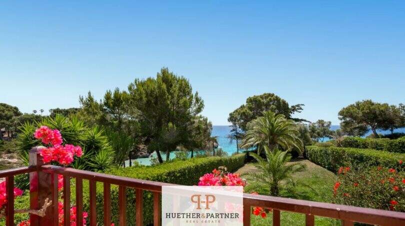 Balcón con barandilla de flores, vista al jardín con palmeras y mar turquesa en primera línea de mar, Cala Mandia