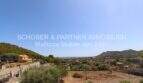 Panoramic view over Son Servera with view of hills, vegetation and sea under blue sky.