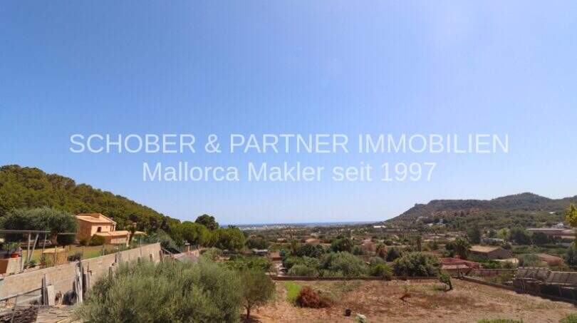 Panoramic view over Son Servera with view of hills, vegetation and sea under blue sky.