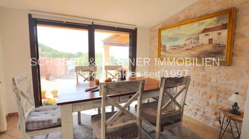 Dining room with rustic wooden table, natural stone wall and large window with panoramic view in Son Servera