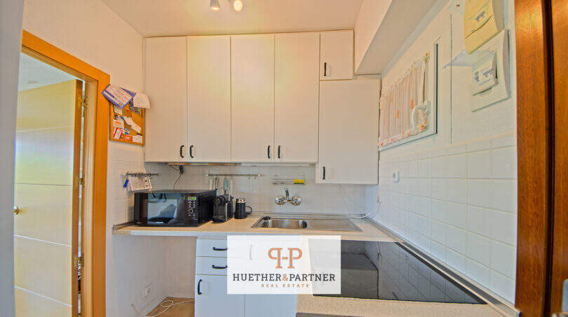 Kleine Einbauküche mit weißen Schränken, Spüle, Mikrowelle und Fliesenspiegel im Apartment in Cales de Mallorca