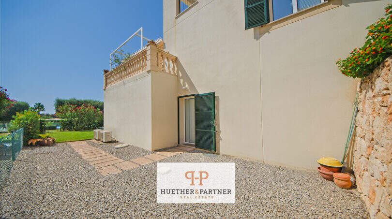 Außenbereich Reiheneckhaus Porto Cristo Novo: Kieselfläche, grüne Fensterläden, Terrasse mit Balustrade und üppiger Gartenbegrünung.