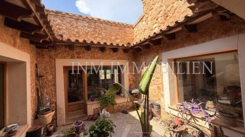 Mediterraner Innenhof der Finca Llucmajor mit Natursteinmauern, Terrakottadach und üppigen Topfpflanzen.