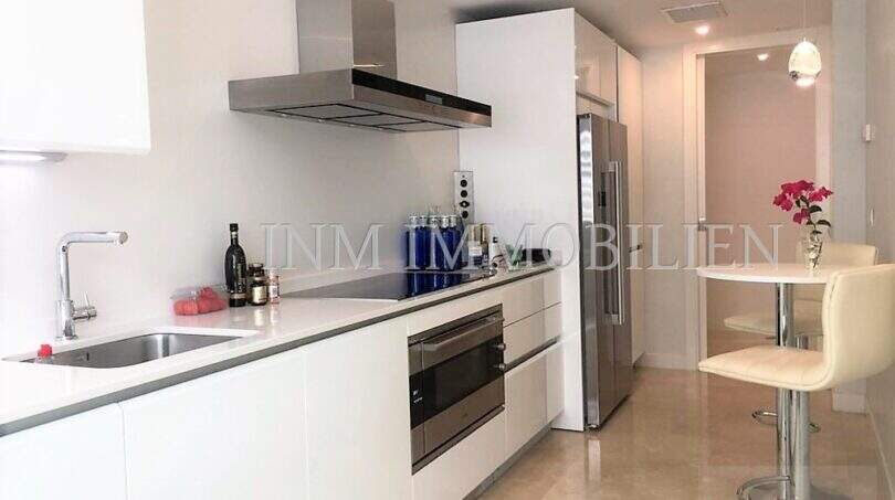 Moderne weiße Einbauküche mit Edelstahl-Dunstabzug, Induktionskochfeld und Frühstücksbar in Luxuswohnung Bendinat