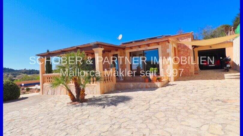 Exterior view Villa Son Servera: Natural stone house with terrace, palm trees, carport and blue sky in Mallorca.