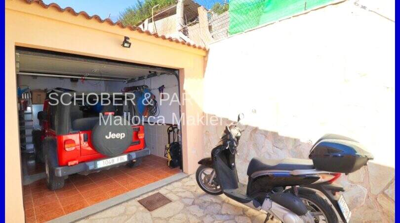 Garage with red Jeep and motor scooter in front of Mediterranean stone house in Son Servera, Mallorca