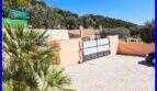 Driveway area of the villa in Son Servera with entrance gate, palm tree and view of wooded hill