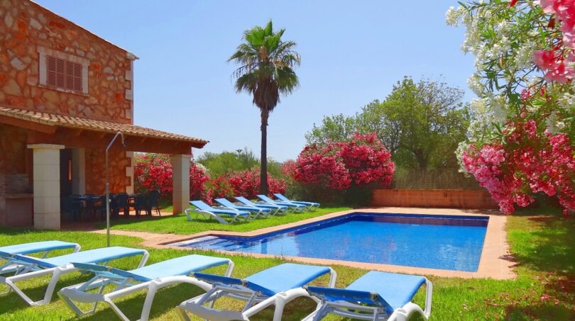 Finca Felanitx: Poolbereich mit Liegestühlen, Palme, blühenden Oleanderbüschen und Natursteinhaus