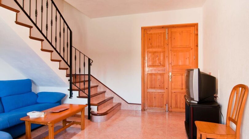 Wohnzimmer der Finca mit blauem Sofa, Holztreppe, rustikaler Holztür und TV in ruhiger Naturlage.