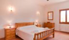 Helles Schlafzimmer der Finca mit Doppelbett, Holzmöbeln, Wandleuchten und Fenster zur Naturlandschaft.