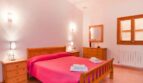 Helles Schlafzimmer der Finca mit Doppelbett, Holzmöbeln, rosa Bettwäsche und Fensterläden.