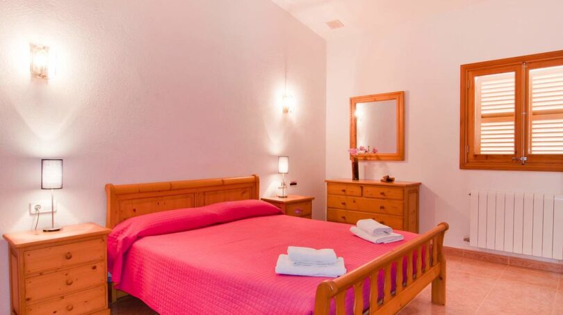 Helles Schlafzimmer der Finca mit Doppelbett, Holzmöbeln, rosa Bettwäsche und Fensterläden.