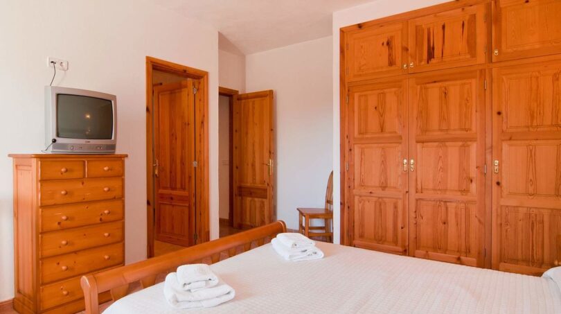 Schlafzimmer der Finca mit Doppelbett, Holzschrank, Kommode und TV in ruhiger Naturlage bei Felanitx.