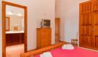 Schlafzimmer der Finca mit Holzmöbeln, CRT-TV, rosa Bett und Blick ins angrenzende Bad