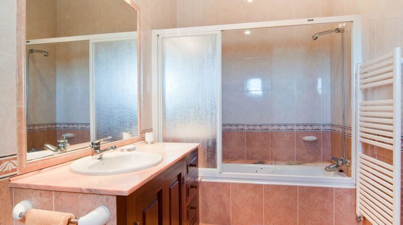 Helles Badezimmer der Finca mit rosa Marmor-Waschtisch, Badewanne mit Glasdusche und Handtuchheizkörper.