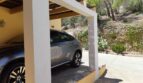 Überdachter Carport der Finca bei Felanitx mit grauem SUV, mediterraner Bepflanzung und Pinien im Hintergrund.