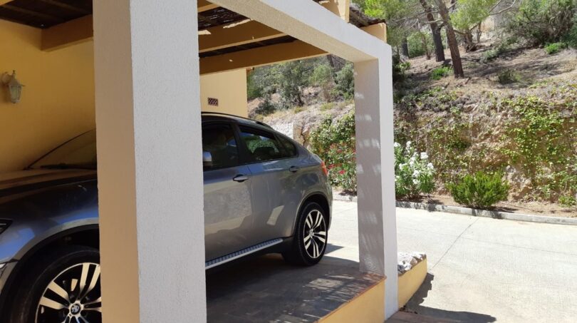 Überdachter Carport der Finca bei Felanitx mit grauem SUV, mediterraner Bepflanzung und Pinien im Hintergrund.