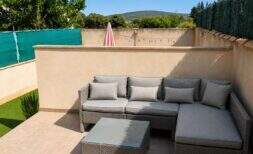 Sunny terrace with gray rattan lounge furniture and string lights, private garden in Santa Maria del Camí