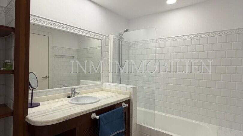 Helles Badezimmer der Dachgeschosswohnung Blanquerna mit Badewanne, Holzwaschtisch und weißen Metrofliesen.