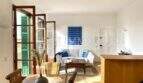 Sala de estar luminosa con sofá blanco, suelo de madera y contraventanas verdes típicas en apartamento del casco antiguo de Palma