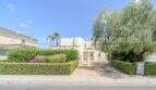 Außenansicht mediterrane Villa in Sa Coma mit gepflegtem Grüngarten, Einfahrt und Palmen unter blauem Himmel.