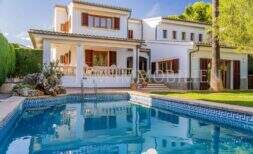 Exterior view of Mediterranean villa Sa Coma with blue pool, white facade, wooden shutters and lush greenery
