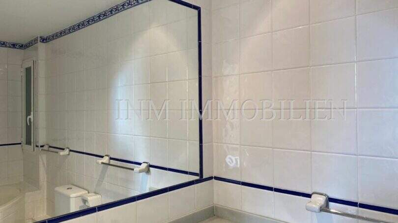Baño luminoso con azulejos blancos, franja decorativa azul, espejo grande y lavabo en apartamento del casco antiguo de Palma