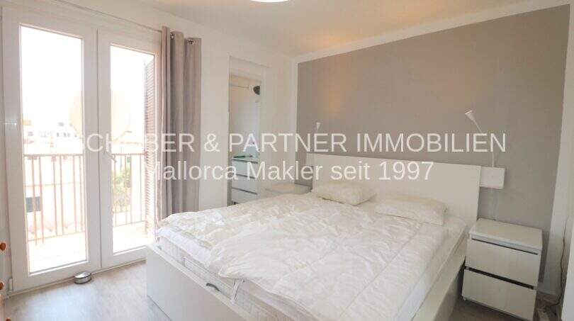 Helles Schlafzimmer mit Doppelbett, grauer Akzentwand und Balkonzugang in modernisierter Wohnung in Cala Ratjada