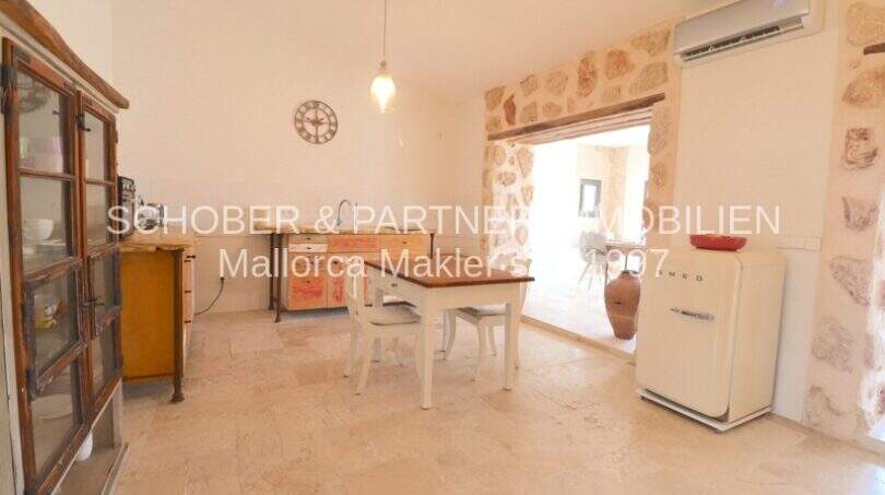 Rustikale Küche mit Natursteinwand, weißem Smeg-Kühlschrank und Esstisch im sanierten Landhaus Portocristo