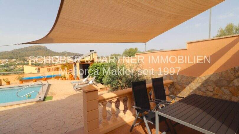Covered terrace with sun sail, dining table, chairs and view of pool and hills in Son Servera