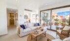 Bright living room with white sofa, rattan furniture and large terrace door with view of sunny terrace in Cala Millor