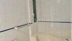 Baño alicatado en blanco con bañera de esquina, inodoro y pequeña ventana en apartamento del casco antiguo de Palma