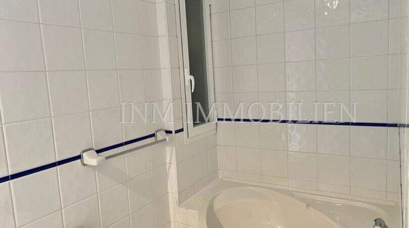 Baño alicatado en blanco con bañera de esquina, inodoro y pequeña ventana en apartamento del casco antiguo de Palma