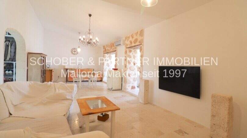Helles Wohnzimmer mit weißen Sofas, Holztisch, Kronleuchter und TV im sanierten Landhaus in Port de Manacor