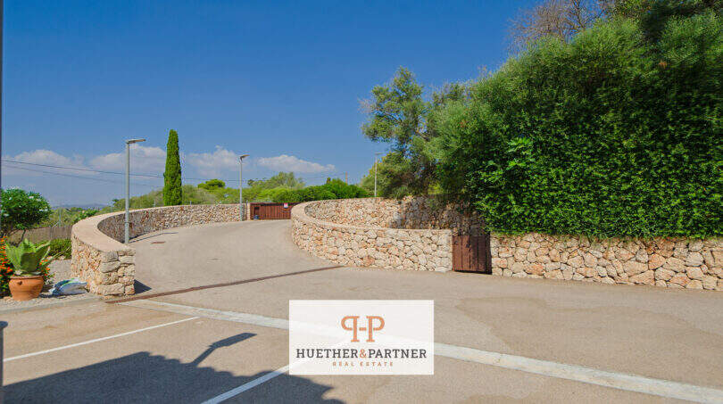 Gepflasterter Einfahrtsbereich des Reiheneckhauses in Porto Cristo Novo mit Natursteinmauern und üppigem Grün.