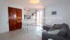 Salón luminoso con sofá gris, mesa de comedor blanca y cocina abierta en apartamento modernizado en Cala Ratjada