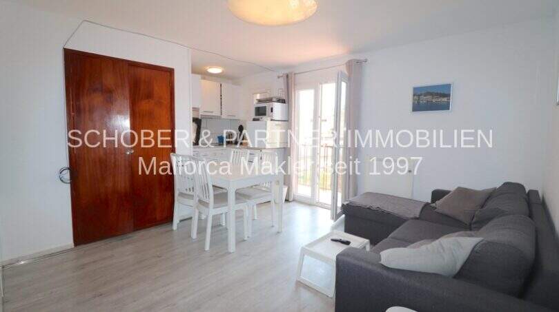 Helles Wohnzimmer mit grauem Sofa, weißem Esstisch und offener Küche in modernisierter Wohnung in Cala Ratjada