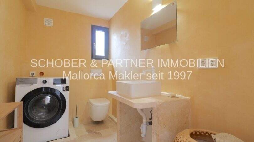 Badezimmer mit Waschmaschine, Wandtoilette und Naturstein-Waschtisch im sanierten Landhaus Port de Manacor