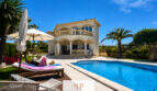 Villa Sa Torre Llucmajor: Mediterrane Außenansicht mit Pool, Sonnenterrasse, Palmen und Balkon unter blauem Himmel.