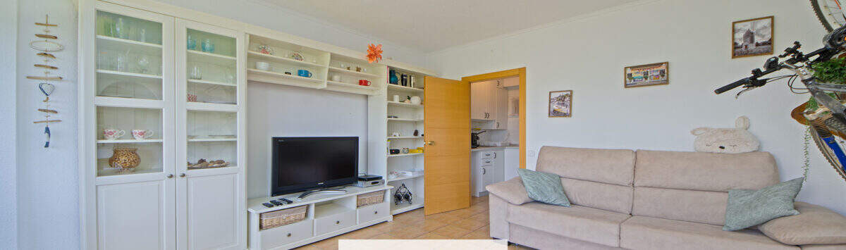 Helles Wohnzimmer mit weißem Regalschrank, TV, Sofa und Blick zur Küche in Apartment Cales de Mallorca