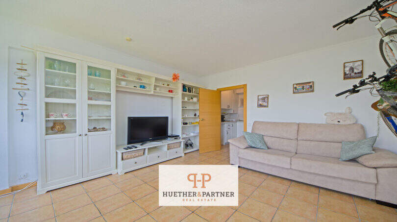 Helles Wohnzimmer mit weißem Regalschrank, TV, Sofa und Blick zur Küche in Apartment Cales de Mallorca