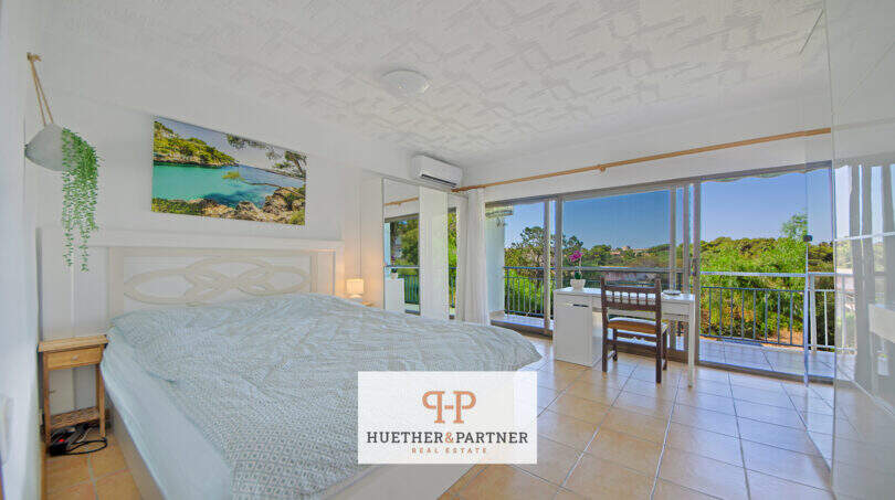 Helles Schlafzimmer mit Doppelbett, Klimaanlage und großer Glasfront mit Balkon und Grünblick in Cales de Mallorca