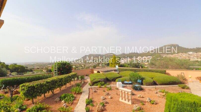 Well-maintained garden with curved hedges, gravel path and panoramic view of mountains and village in Son Servera