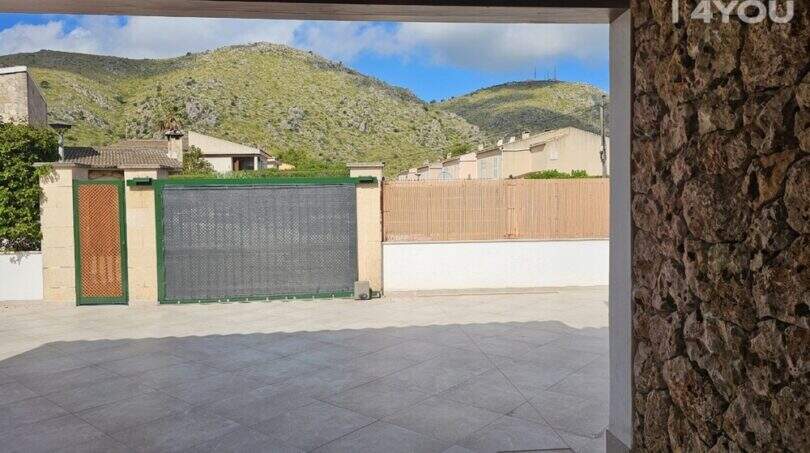 Überdachte Einfahrt mit Natursteinwand, grauem Fliesenboden und elektrischem Tor mit Blick auf die Tramuntana-Berge.