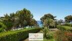 Gepflegter Garten mit Hecken, Palmen und Blick auf die türkisblaue Bucht Cala Mandia in erster Meereslinie.