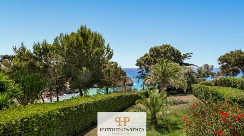Cuidado jardín con setos, palmeras y vista a la cala turquesa de Cala Mandia en primera línea de mar.