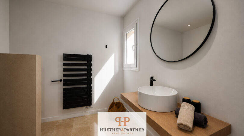 Modernes Badezimmer der Villa in Sa Torre mit rundem Spiegel, Aufsatzwaschbecken und schwarzem Heizkörper