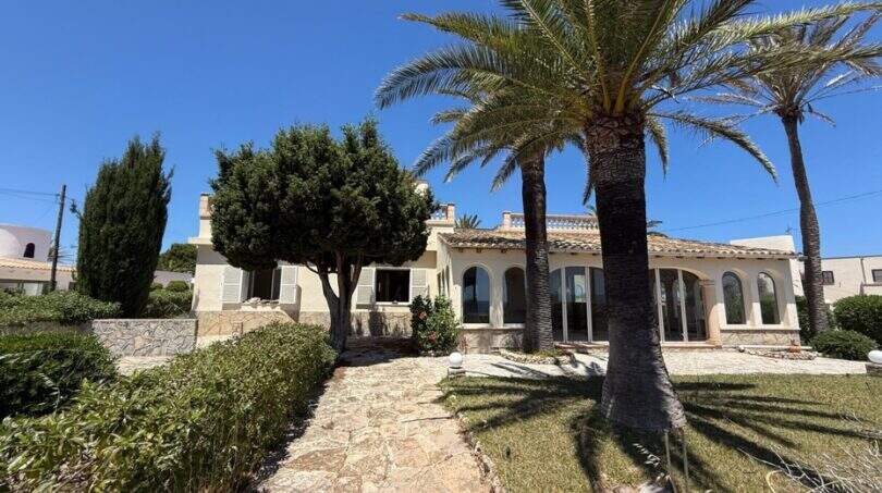 Mediterrane Villa in Cala Murada mit Palmen, Steinweg und gepflegtem Garten unter blauem Himmel.